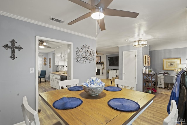 dining space with crown molding, ceiling fan with notable chandelier, sink, and light wood-type flooring