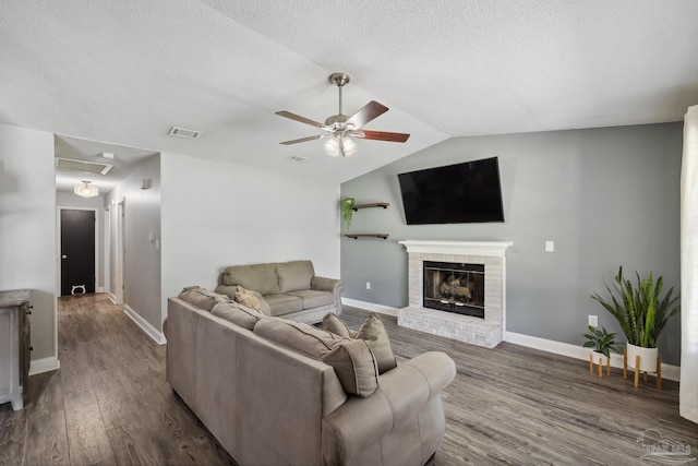 living room with hardwood / wood-style flooring, vaulted ceiling, a fireplace, a textured ceiling, and ceiling fan