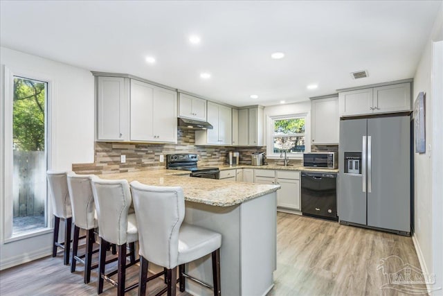 kitchen with black appliances, a breakfast bar, kitchen peninsula, and light stone counters