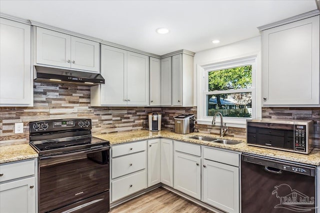 kitchen featuring light hardwood / wood-style floors, decorative backsplash, black appliances, light stone counters, and sink