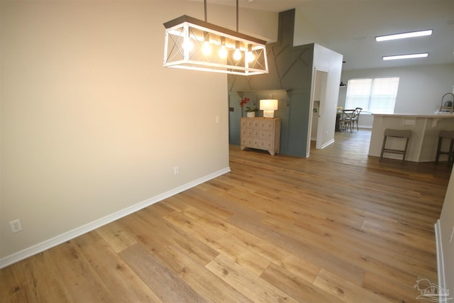unfurnished dining area with a chandelier, light wood-style floors, and baseboards