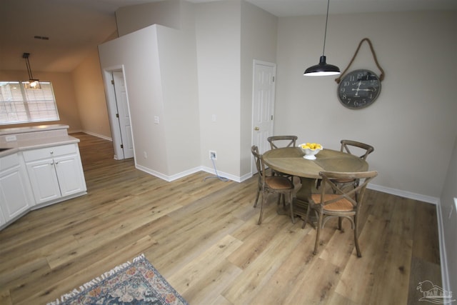 dining space featuring visible vents, baseboards, light wood-style floors, and lofted ceiling
