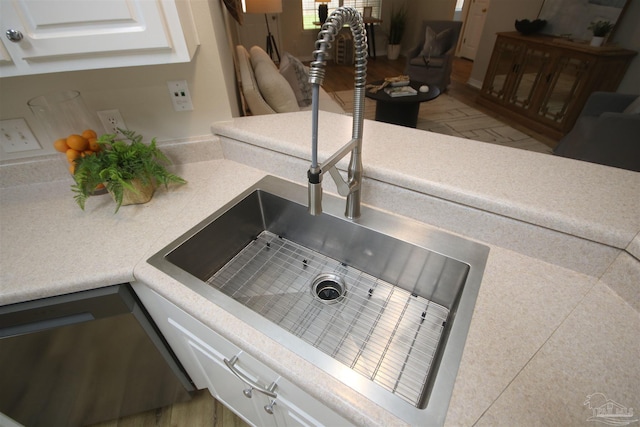 room details with white cabinetry, wood finished floors, dishwasher, light countertops, and a sink