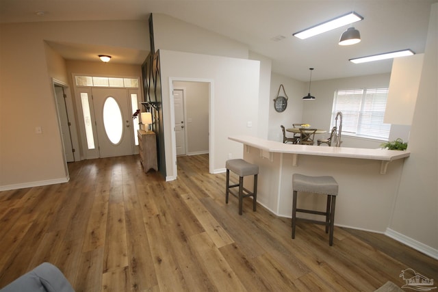 kitchen featuring a kitchen breakfast bar, light wood-style flooring, a peninsula, light countertops, and lofted ceiling