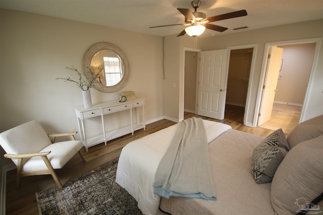 bedroom with a walk in closet, visible vents, baseboards, and wood finished floors