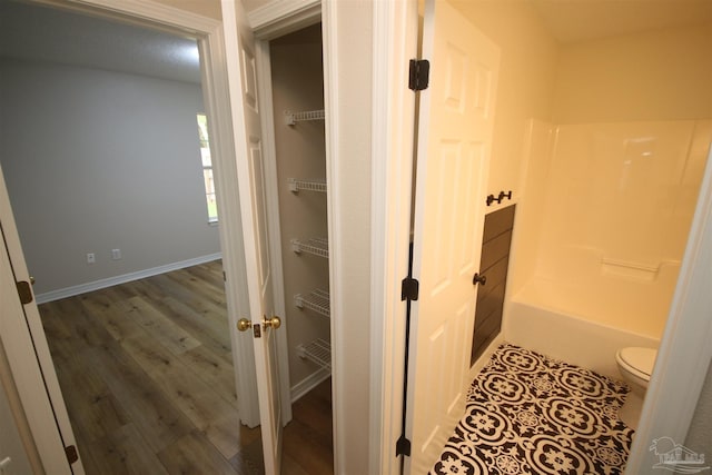 bathroom with toilet, wood finished floors, baseboards, and shower / bathtub combination