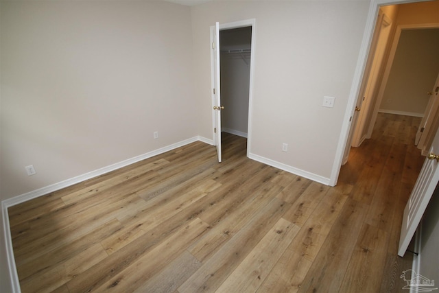 unfurnished bedroom featuring a closet, a spacious closet, light wood-style floors, and baseboards