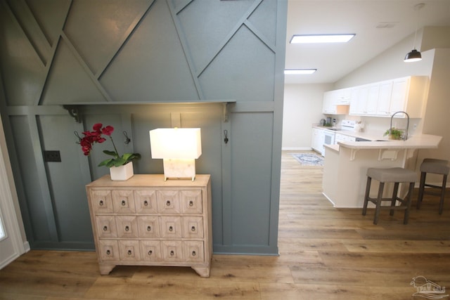 hall featuring a sink, light wood-type flooring, and vaulted ceiling