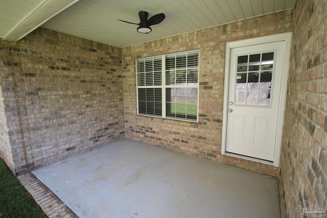 view of exterior entry with brick siding, a ceiling fan, and a patio area
