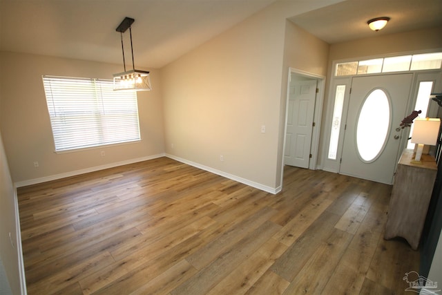 entryway with baseboards, vaulted ceiling, a chandelier, and wood finished floors