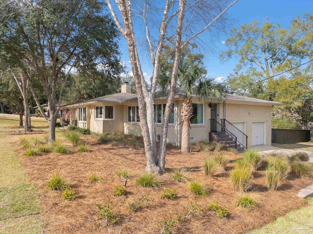 single story home with a garage, driveway, a chimney, and brick siding