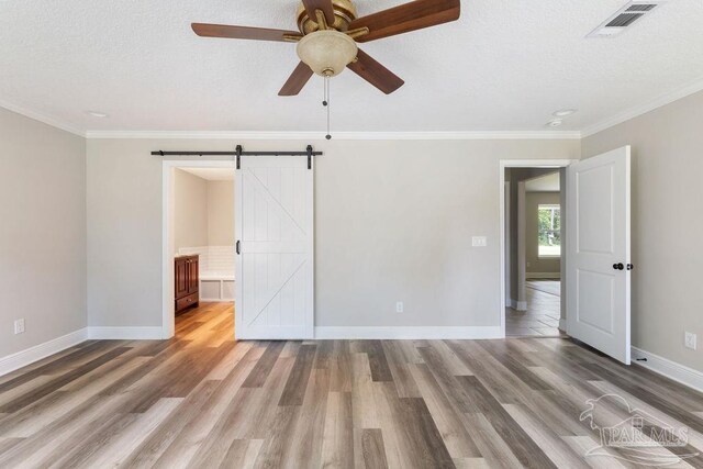 9317 Alekai Dr, Pensacola, FL 32526 - unfurnished bedroom with a barn door, wood finished floors, a textured ceiling, crown molding, and a ceiling fan