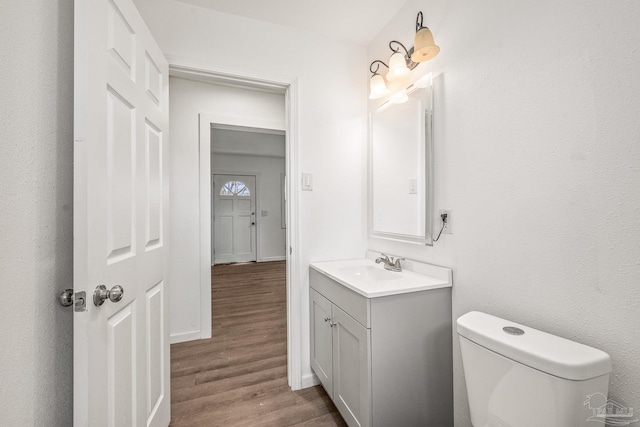 bathroom with vanity, toilet, wood finished floors, and baseboards