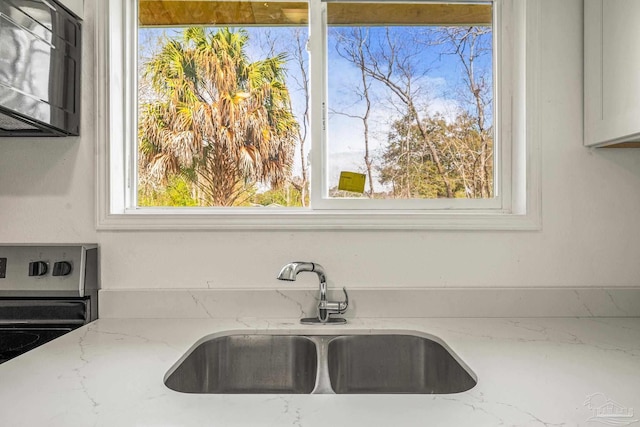 kitchen with light stone counters, stainless steel range with electric cooktop, and a sink