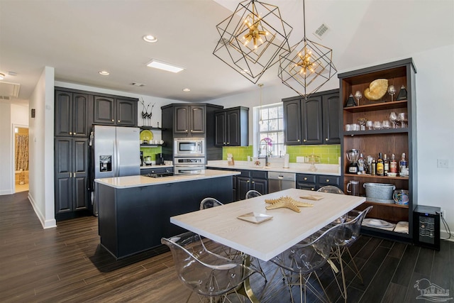 kitchen featuring dark wood-style flooring, appliances with stainless steel finishes, a center island, light countertops, and an inviting chandelier