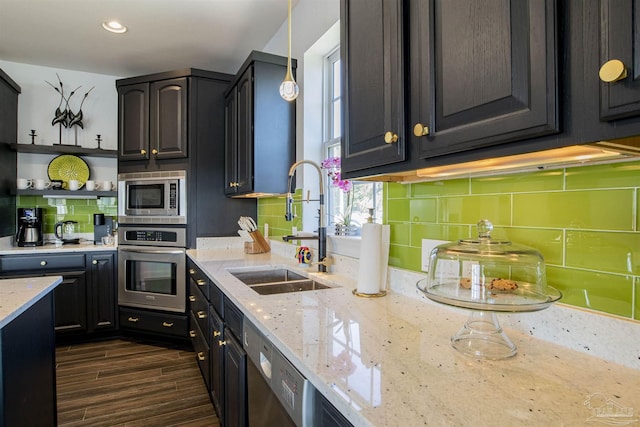 kitchen featuring light stone counters, a sink, stainless steel appliances, dark wood-type flooring, and backsplash