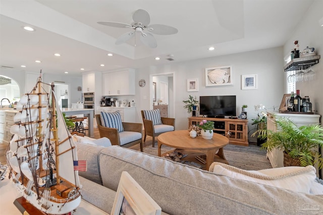 living room featuring sink, ceiling fan, and a tray ceiling