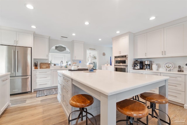 kitchen with white cabinets, a kitchen bar, a center island, stainless steel appliances, and light hardwood / wood-style flooring