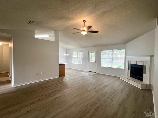 4888 La Casa Cir, Pace, FL 32571 - unfurnished living room featuring a ceiling fan, vaulted ceiling, a textured ceiling, a tiled fireplace, and dark wood finished floors