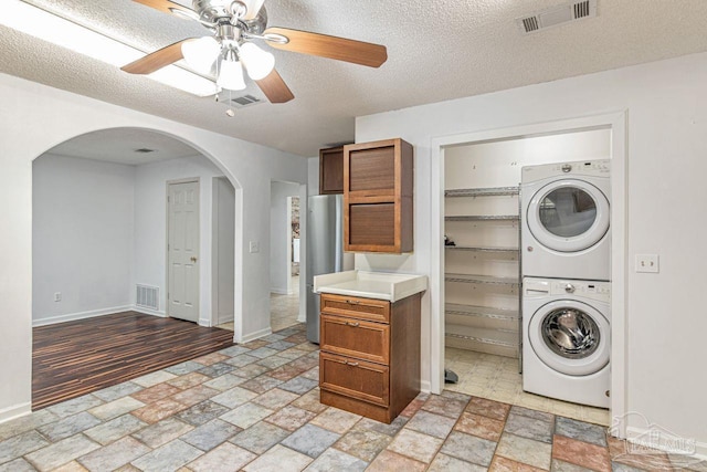 10449 Bernice Rd, Milton, FL 32583 - washroom featuring stacked washer and clothes dryer, arched walkways, stone tile floors, baseboards, and ceiling fan