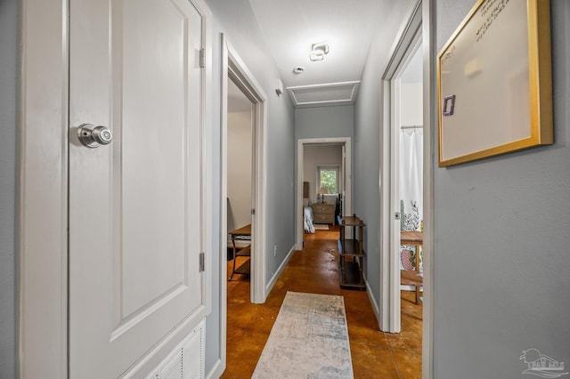 hallway featuring finished concrete floors, attic access, and baseboards