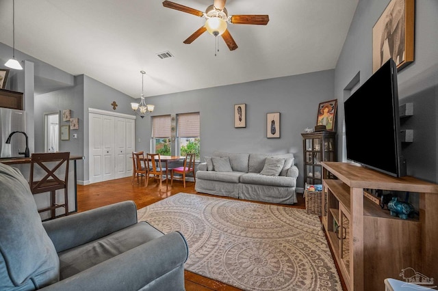 living room featuring ceiling fan with notable chandelier, vaulted ceiling, wood finished floors, and visible vents