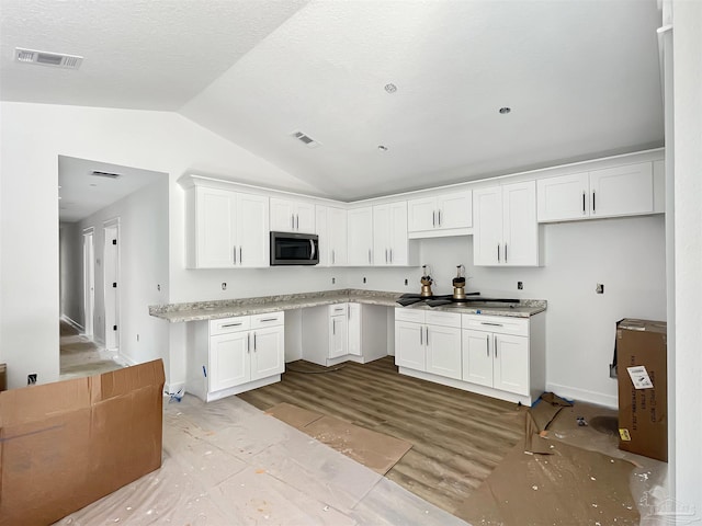 kitchen featuring wood finished floors, visible vents, white cabinetry, vaulted ceiling, and stainless steel microwave