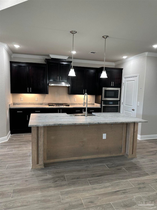 kitchen with hanging light fixtures, sink, a kitchen island with sink, stainless steel appliances, and light stone countertops