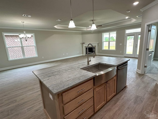 kitchen featuring an island with sink, a raised ceiling, light hardwood / wood-style flooring, stainless steel dishwasher, and sink