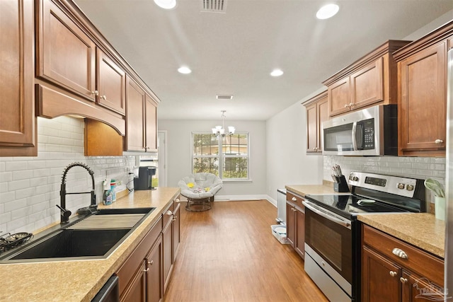 kitchen featuring light hardwood / wood-style floors, stainless steel appliances, sink, a chandelier, and backsplash