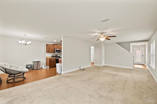 unfurnished living room featuring ceiling fan with notable chandelier and light hardwood / wood-style flooring