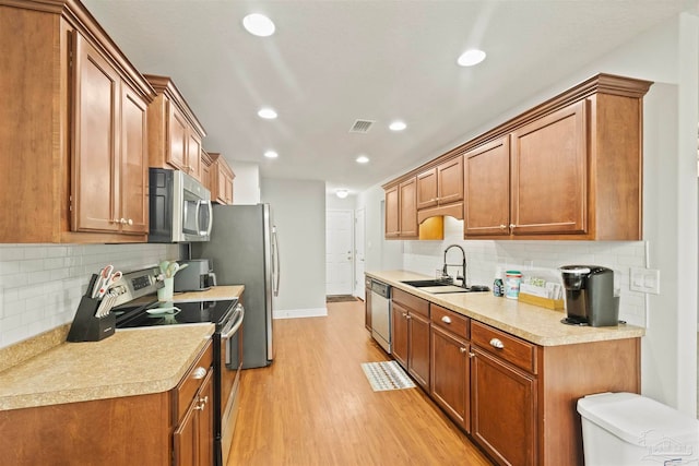 kitchen with light hardwood / wood-style floors, sink, backsplash, and appliances with stainless steel finishes