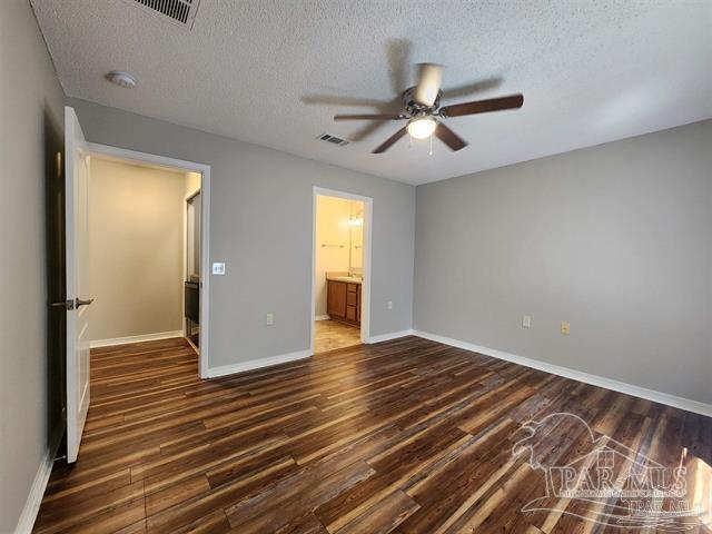 unfurnished bedroom featuring ceiling fan, dark hardwood / wood-style flooring, a textured ceiling, and ensuite bath