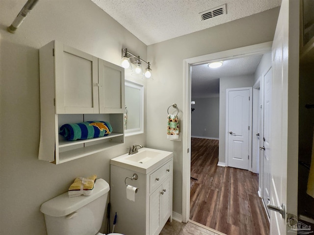 bathroom with vanity, toilet, wood-type flooring, and a textured ceiling