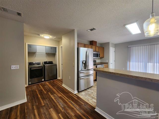 kitchen featuring washer and clothes dryer, dark hardwood / wood-style flooring, stainless steel appliances, and a textured ceiling