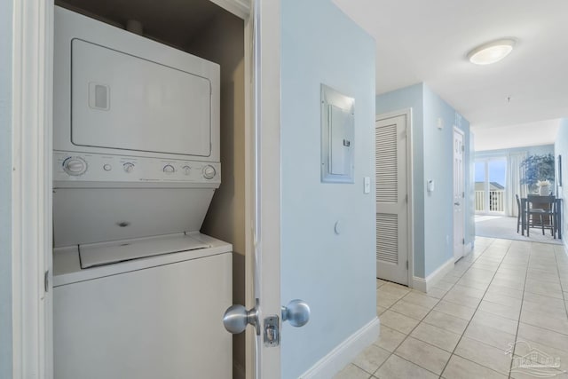 laundry area featuring light tile patterned flooring, stacked washing maching and dryer, and electric panel