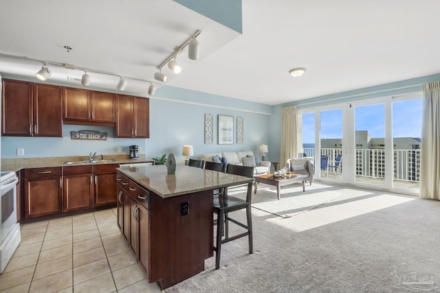 kitchen with a kitchen bar, sink, a center island, light tile patterned floors, and light stone countertops