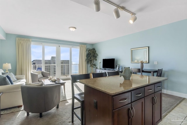 kitchen with a breakfast bar area, light stone counters, dark brown cabinets, track lighting, and a kitchen island