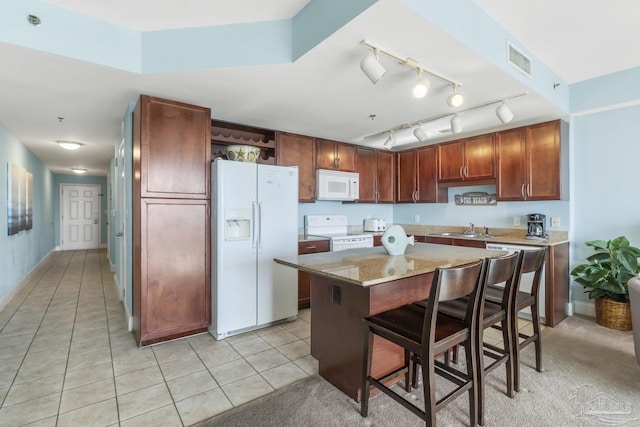 kitchen featuring sink, a kitchen bar, a center island, light tile patterned floors, and white appliances