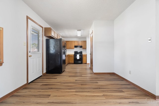 kitchen featuring black appliances, light hardwood / wood-style floors, a textured ceiling, and range hood