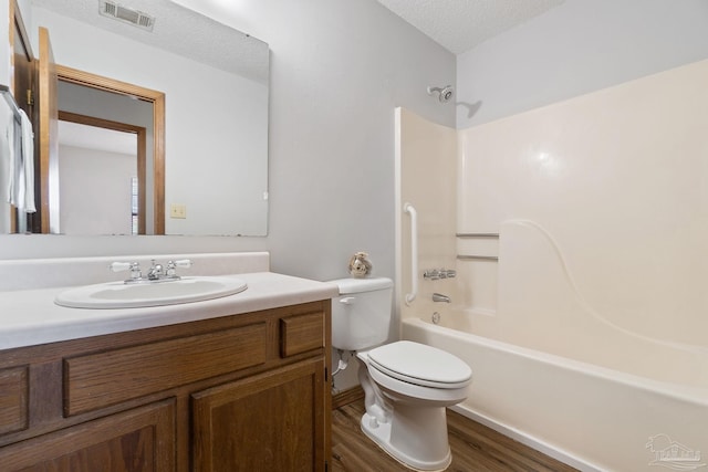 full bathroom with shower / bathing tub combination, a textured ceiling, hardwood / wood-style floors, toilet, and vanity