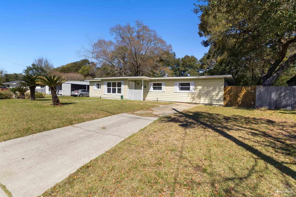 ranch-style home with concrete driveway, fence, and a front lawn