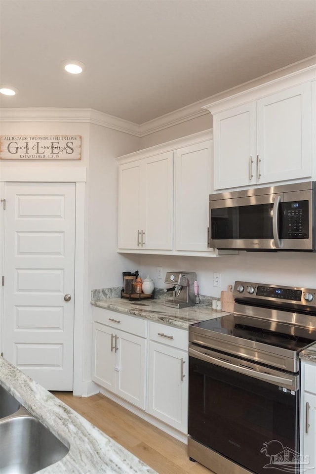 kitchen with light stone countertops, light wood-type flooring, stainless steel appliances, crown molding, and white cabinets