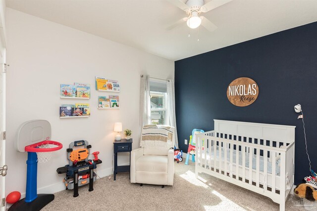 carpeted bedroom featuring ceiling fan and a crib