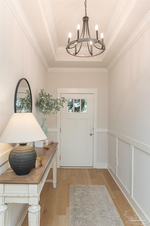 foyer entrance featuring a tray ceiling, an inviting chandelier, crown molding, and light hardwood / wood-style floors