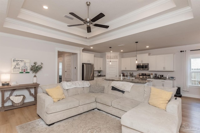 living room with ceiling fan, light hardwood / wood-style floors, ornamental molding, and a tray ceiling