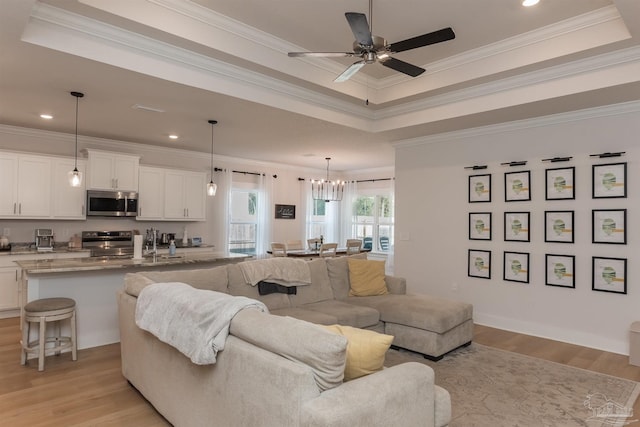 living room featuring a raised ceiling, light hardwood / wood-style floors, ceiling fan with notable chandelier, and ornamental molding