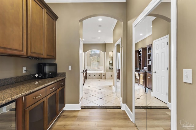 kitchen with beverage cooler, light tile patterned flooring, dark stone counters, and ornamental molding