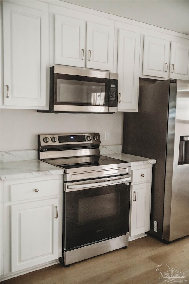 kitchen with appliances with stainless steel finishes, light hardwood / wood-style floors, white cabinets, and light stone countertops