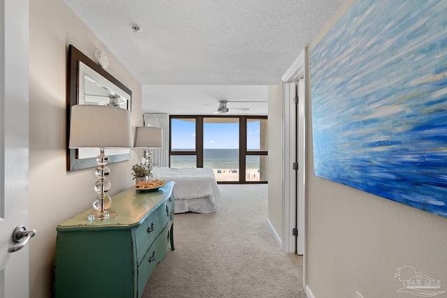 hallway with a water view, light colored carpet, and a textured ceiling